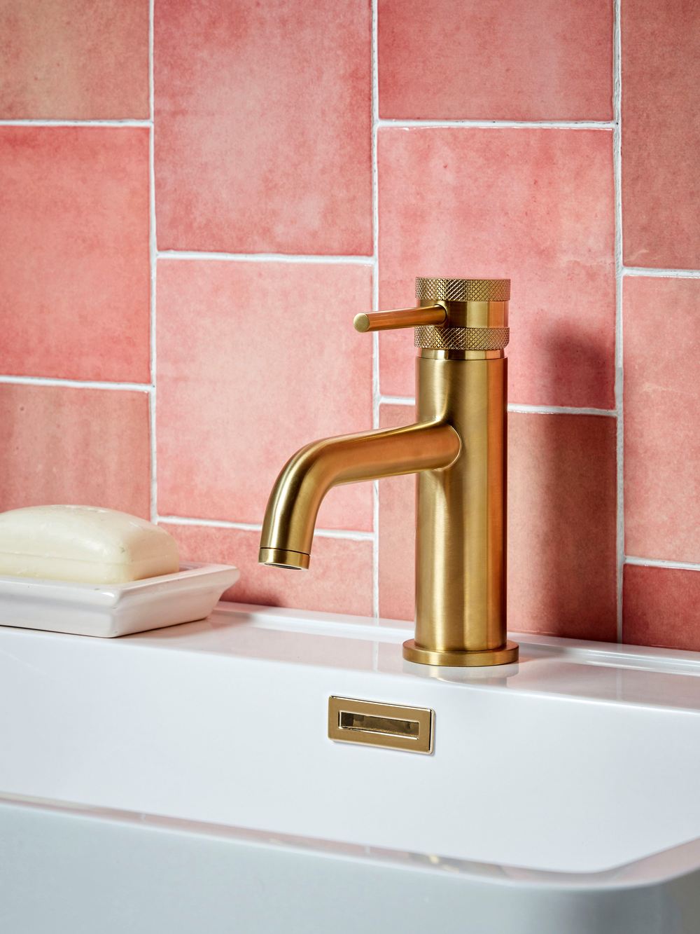 Brushed brass basin tap against warm pink tiles